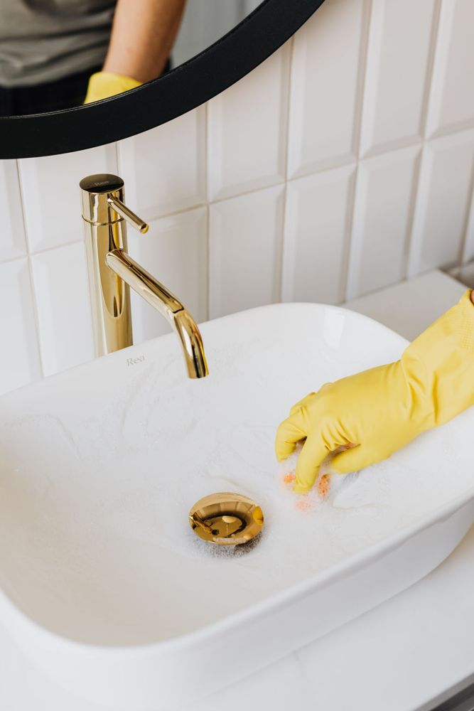 Gloved hand cleaning a bathroom sink and faucet