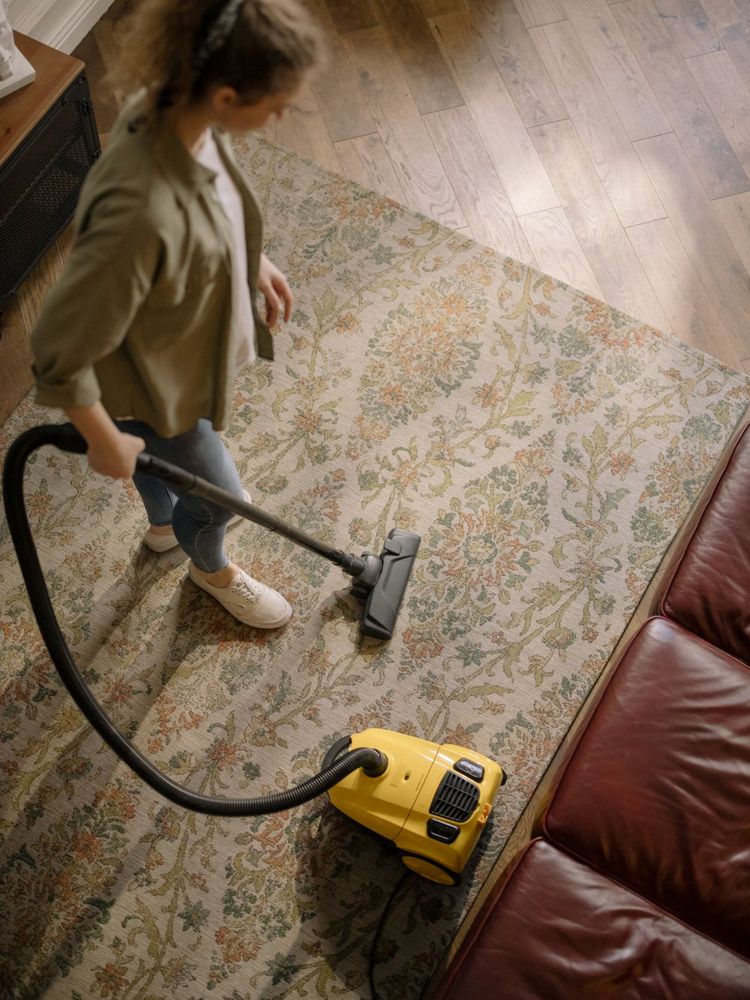 Person vacuuming a patterned carpet in a living room