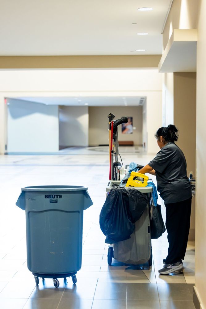 Commercial janitor with cleaning cart in a bright office hallway