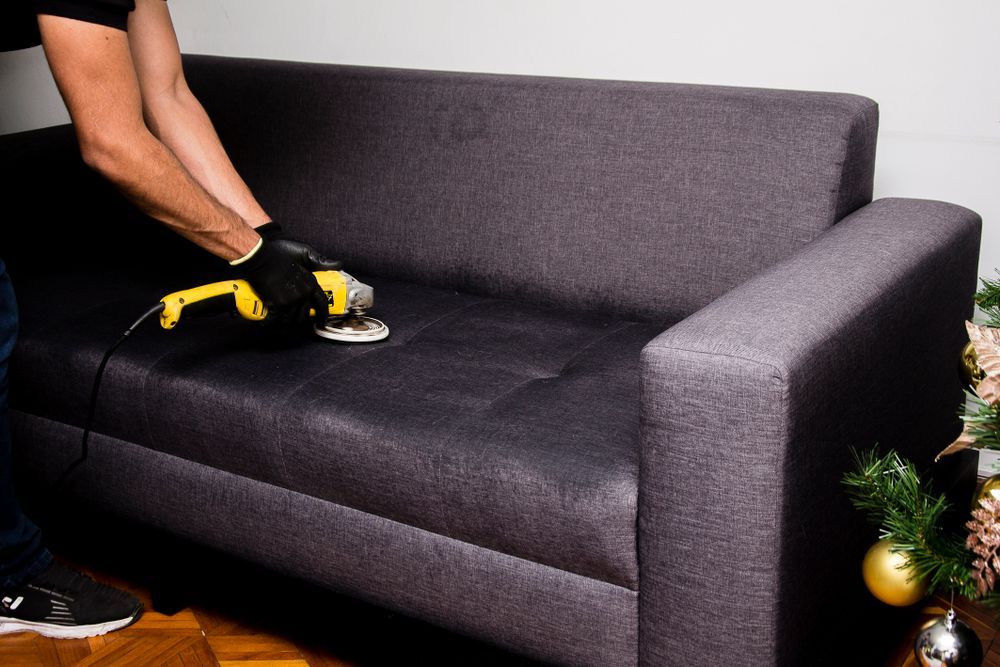 Technician cleaning a dark fabric sofa with upholstery equipment